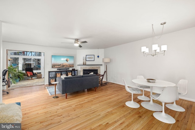 dining space featuring ceiling fan with notable chandelier, light hardwood / wood-style floors, and a tiled fireplace