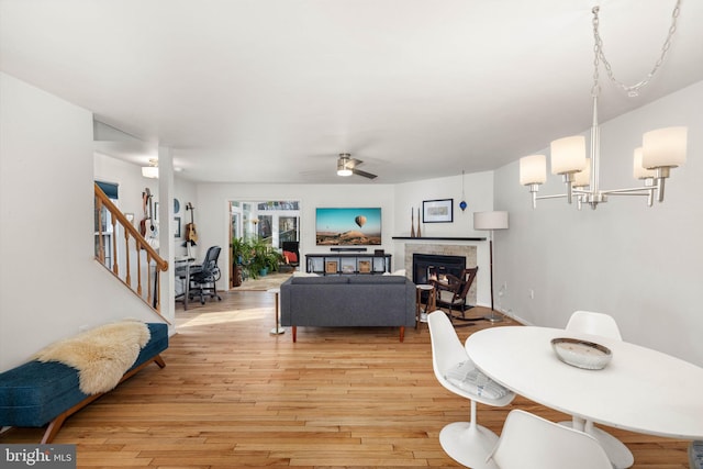 living room with ceiling fan with notable chandelier, a tiled fireplace, and light hardwood / wood-style flooring