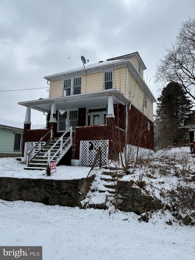 snow covered house featuring covered porch