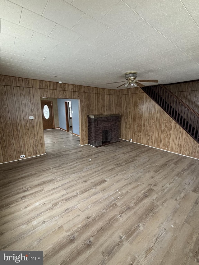 unfurnished living room with hardwood / wood-style floors, a brick fireplace, ceiling fan, and wooden walls