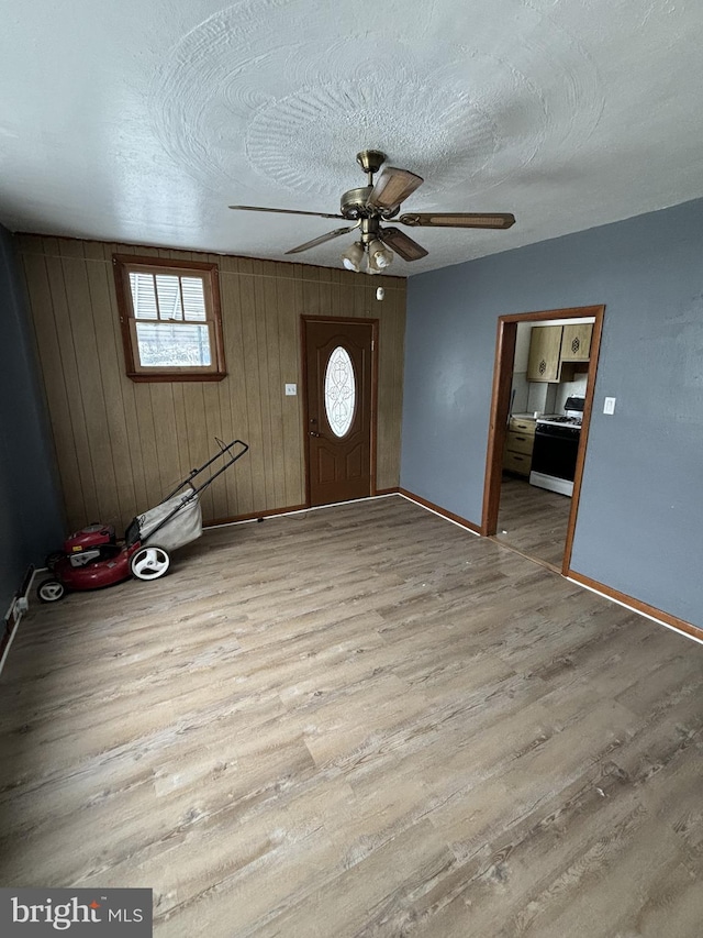 entryway featuring a textured ceiling, light hardwood / wood-style floors, ceiling fan, and wood walls