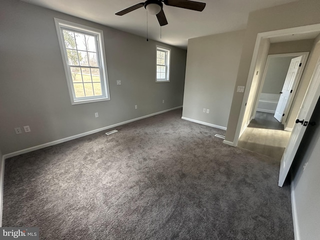 spare room featuring ceiling fan, a healthy amount of sunlight, and dark colored carpet