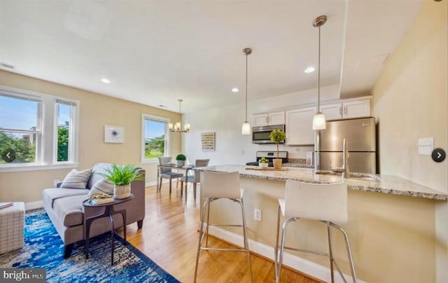 kitchen featuring light stone countertops, a kitchen breakfast bar, pendant lighting, white cabinets, and appliances with stainless steel finishes