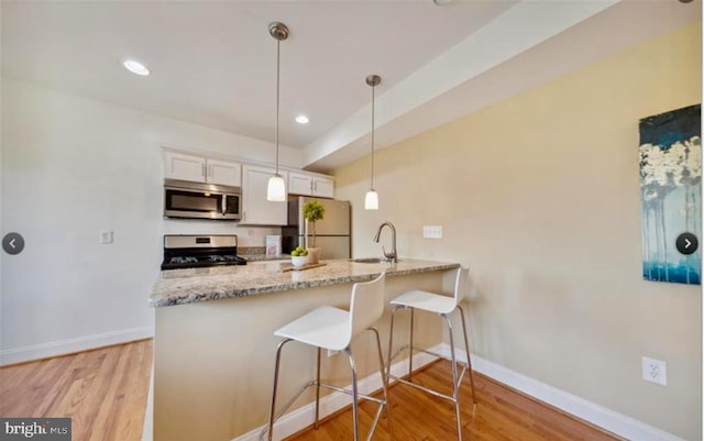 kitchen featuring sink, kitchen peninsula, decorative light fixtures, white cabinets, and appliances with stainless steel finishes