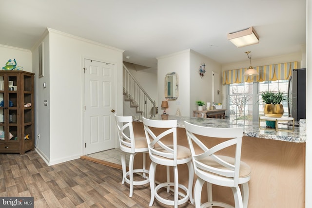 kitchen featuring light stone counters, decorative light fixtures, ornamental molding, kitchen peninsula, and hardwood / wood-style floors