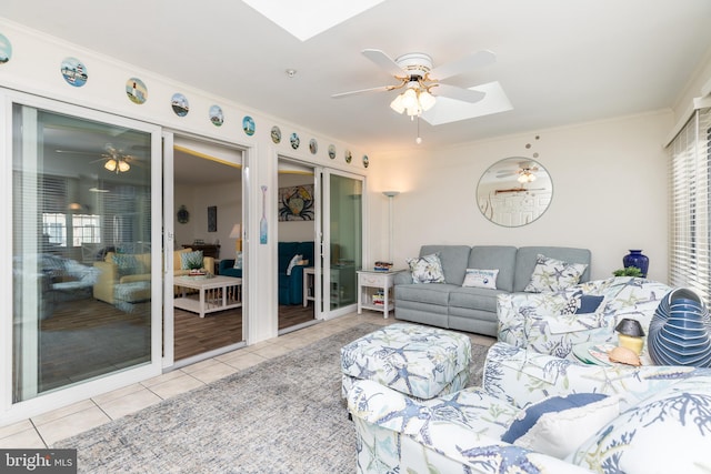 living room featuring light tile patterned floors, crown molding, a skylight, and ceiling fan