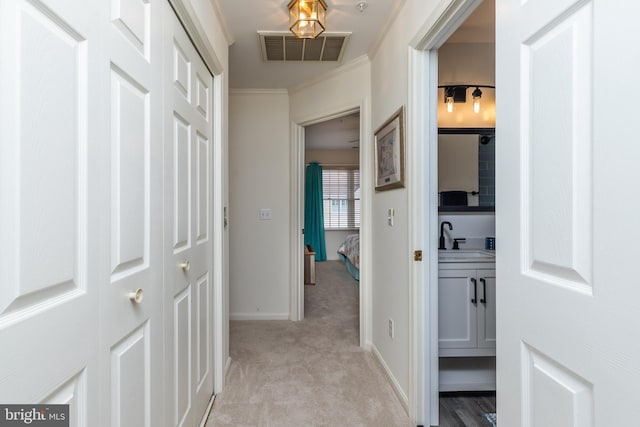 corridor featuring ornamental molding, sink, and light carpet