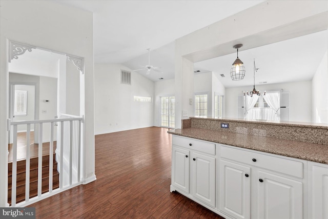 kitchen featuring pendant lighting, dark stone counters, ceiling fan with notable chandelier, vaulted ceiling, and white cabinetry