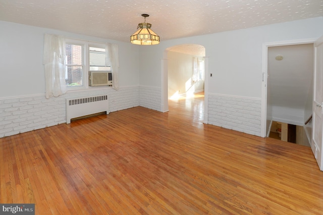 empty room featuring arched walkways, radiator, brick wall, wood finished floors, and a textured ceiling