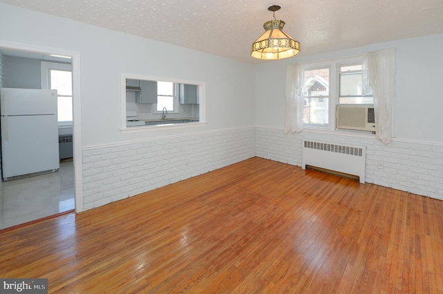 interior space featuring a textured ceiling, cooling unit, hardwood / wood-style flooring, brick wall, and radiator