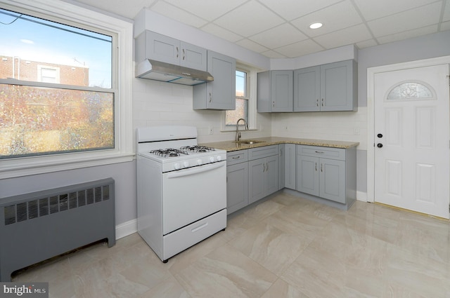 kitchen featuring under cabinet range hood, a sink, white range with gas cooktop, gray cabinets, and radiator heating unit