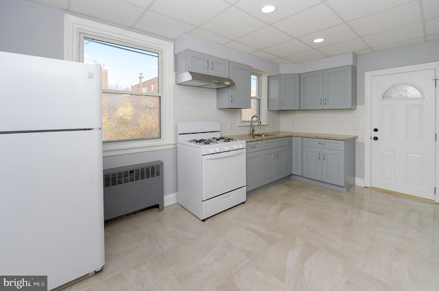 kitchen featuring under cabinet range hood, white appliances, a sink, gray cabinets, and radiator heating unit