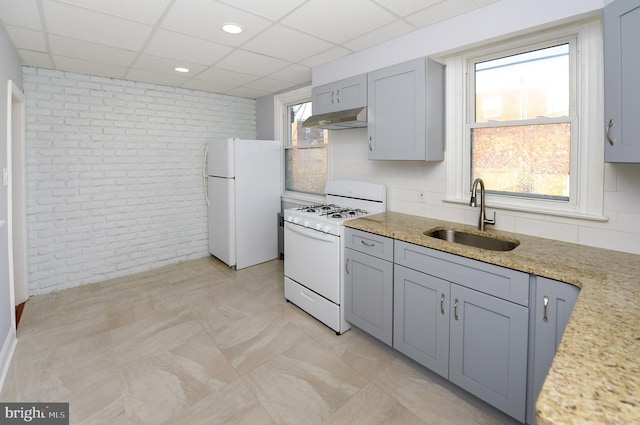 kitchen with white appliances, brick wall, a paneled ceiling, under cabinet range hood, and a sink