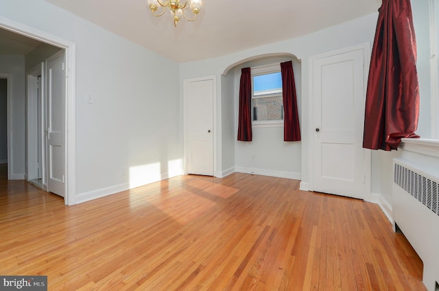 spare room with baseboards, arched walkways, radiator heating unit, light wood-style flooring, and a chandelier