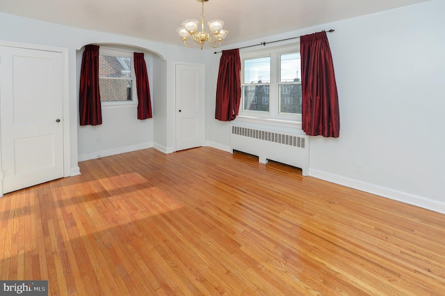 spare room with radiator, a notable chandelier, light wood-style flooring, and baseboards