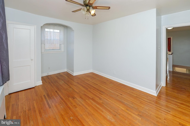 spare room with light wood-type flooring, arched walkways, baseboards, and a ceiling fan