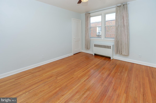 spare room with radiator, light wood finished floors, baseboards, and a ceiling fan