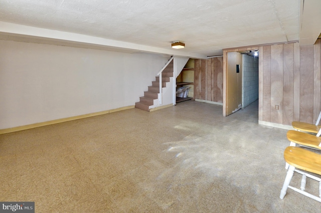 finished basement with wood walls, a textured ceiling, baseboards, and stairs