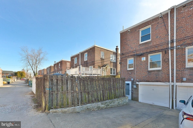 exterior space featuring an attached garage, brick siding, fence, driveway, and a residential view