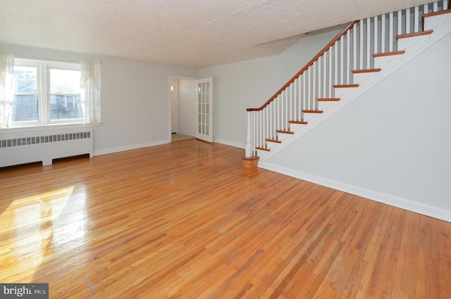 unfurnished living room with a textured ceiling, baseboards, stairs, radiator, and hardwood / wood-style floors