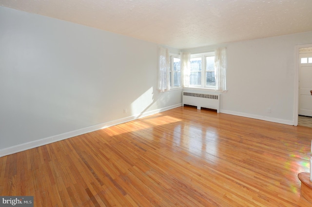 empty room featuring radiator, light wood-type flooring, baseboards, and a textured ceiling