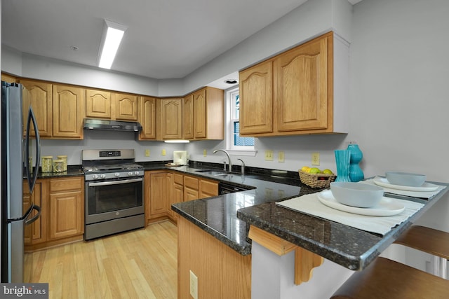 kitchen featuring kitchen peninsula, dark stone counters, stainless steel appliances, sink, and a breakfast bar area