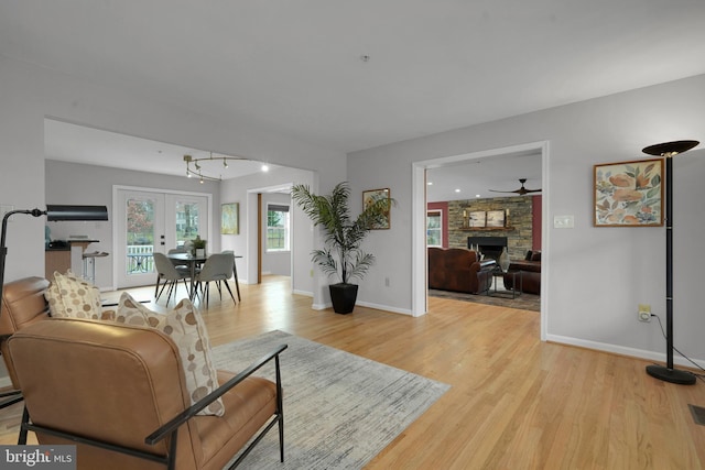 living room featuring french doors, light wood-type flooring, a stone fireplace, and ceiling fan