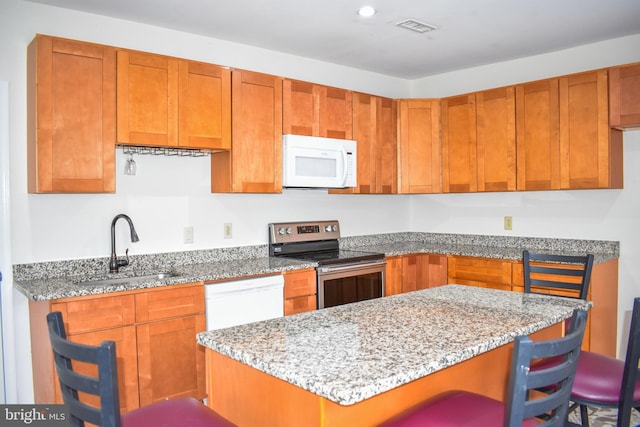 kitchen with light stone counters, sink, white appliances, and a breakfast bar