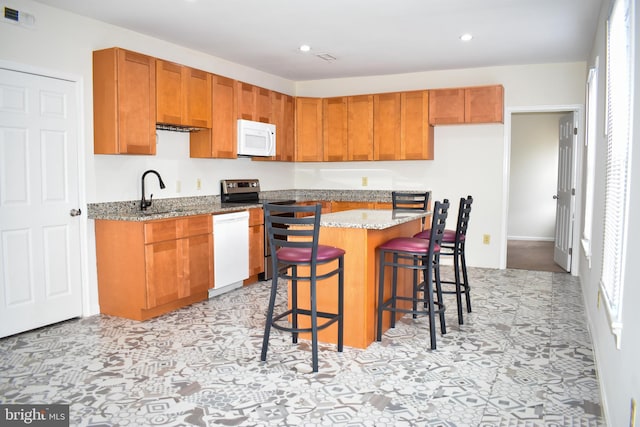 kitchen featuring sink, a breakfast bar area, a center island, light stone counters, and white appliances