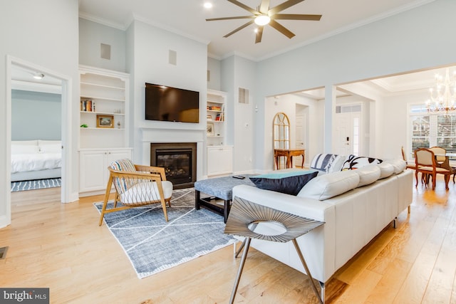 living room featuring built in shelves, light hardwood / wood-style floors, ornamental molding, and ceiling fan with notable chandelier