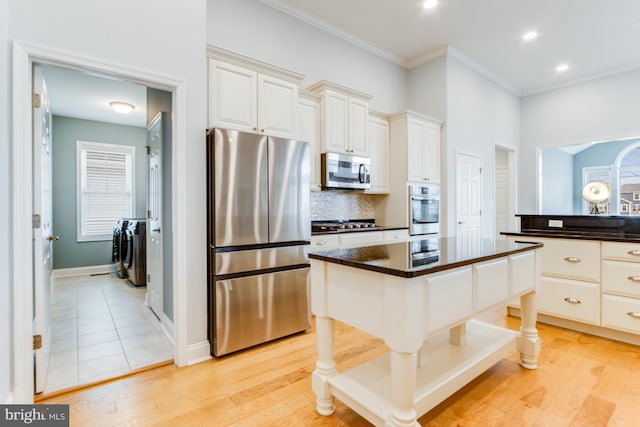 kitchen with washer and clothes dryer, white cabinets, light hardwood / wood-style flooring, a kitchen island, and stainless steel appliances