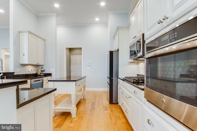 kitchen featuring light wood-type flooring, stainless steel appliances, crown molding, a high ceiling, and white cabinetry