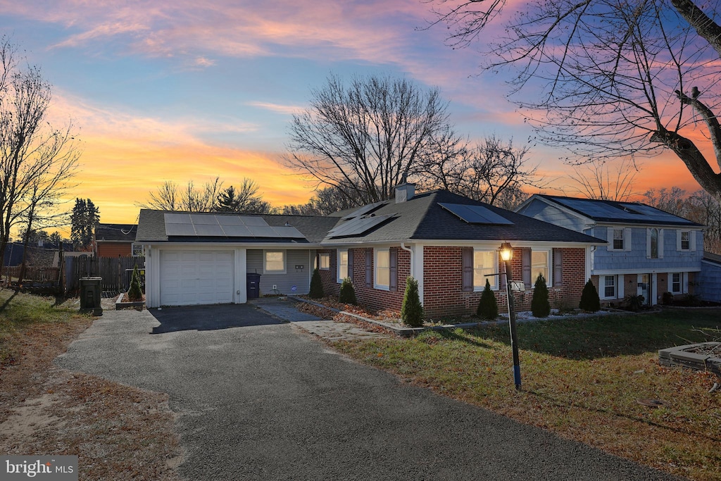 ranch-style house with solar panels, a garage, and a lawn