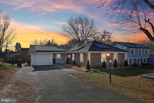 ranch-style house with solar panels, a garage, and a lawn