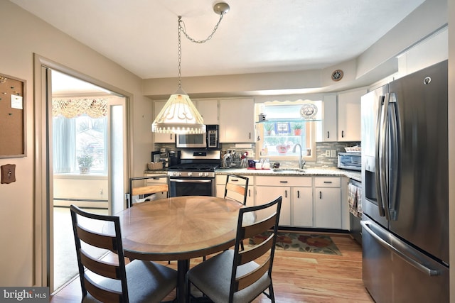 kitchen featuring pendant lighting, appliances with stainless steel finishes, a baseboard heating unit, decorative backsplash, and sink