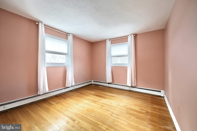 unfurnished room featuring hardwood / wood-style flooring, a baseboard heating unit, and a healthy amount of sunlight