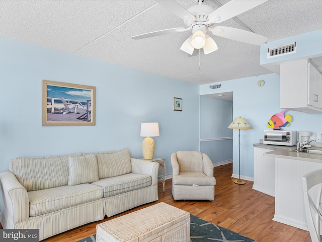 living room with ceiling fan, sink, light hardwood / wood-style floors, and a textured ceiling