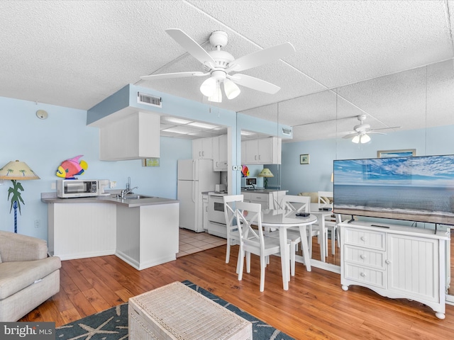 kitchen featuring sink, light hardwood / wood-style flooring, kitchen peninsula, white appliances, and white cabinets