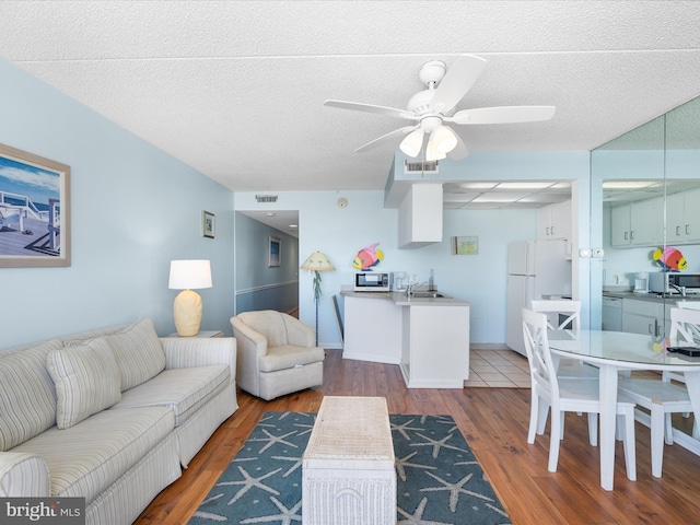 living room featuring ceiling fan, sink, a textured ceiling, and dark wood-type flooring