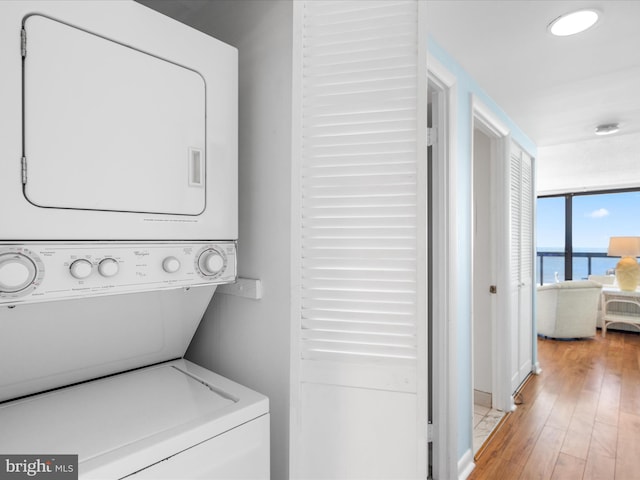 washroom with light hardwood / wood-style floors, a water view, and stacked washing maching and dryer