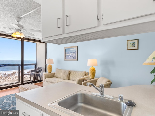 kitchen with white cabinetry, sink, ceiling fan, a textured ceiling, and a water view