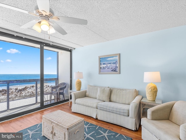 living room with ceiling fan, expansive windows, a textured ceiling, a water view, and hardwood / wood-style flooring