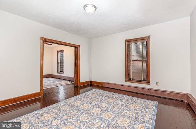 unfurnished room featuring dark hardwood / wood-style flooring and a baseboard heating unit