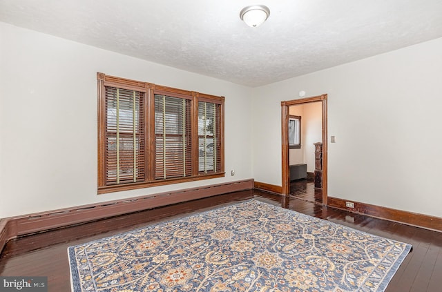 spare room with a textured ceiling, dark hardwood / wood-style flooring, and a baseboard heating unit