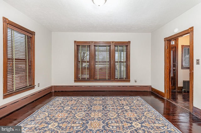 empty room featuring a textured ceiling, dark hardwood / wood-style floors, a baseboard radiator, and radiator