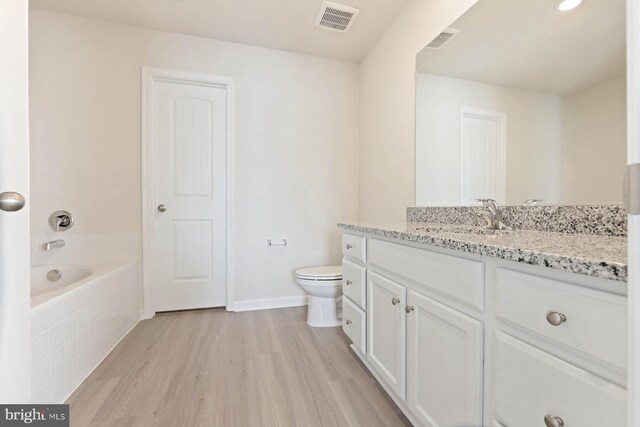 bathroom with hardwood / wood-style floors, vanity, a tub to relax in, and toilet