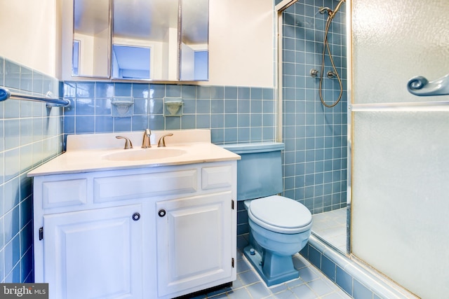 bathroom with toilet, tile walls, vanity, a shower with door, and tile patterned flooring