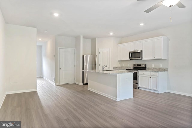 kitchen with white cabinets, sink, light stone countertops, an island with sink, and stainless steel appliances