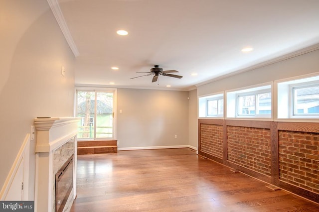 unfurnished living room featuring ceiling fan, crown molding, brick wall, and hardwood / wood-style flooring