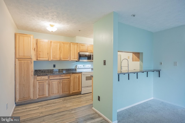 kitchen featuring light hardwood / wood-style flooring, white range with electric stovetop, dark stone countertops, a textured ceiling, and light brown cabinetry